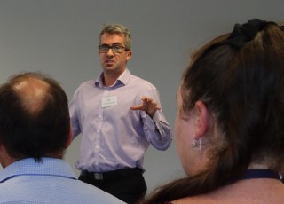 Morgan Strong in front of a room delivering a speech to a group with heads seen in the foreground